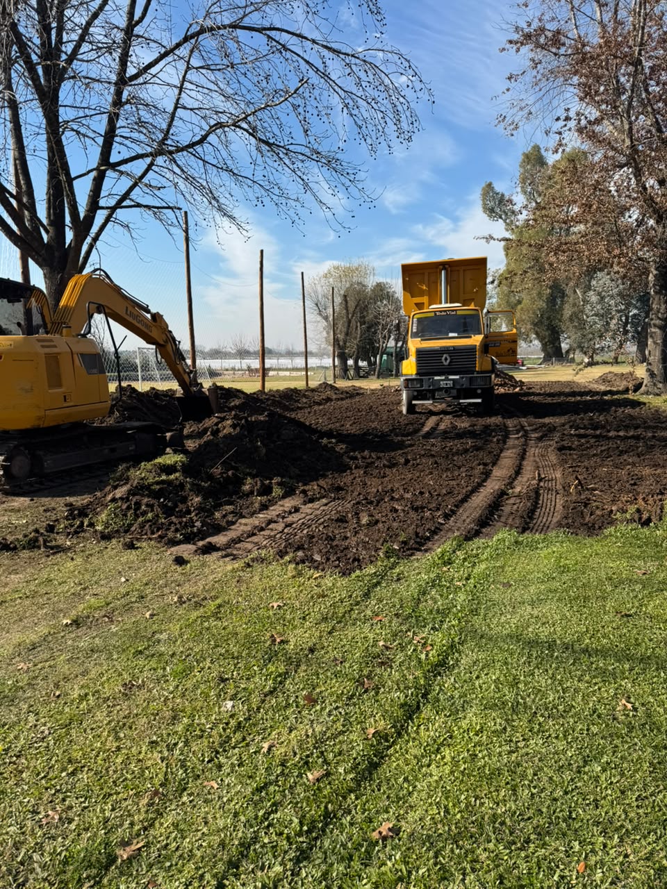 Excavadora LiuGong y camión volcador de Todo Vial removiendo tierra en un predio arbolado