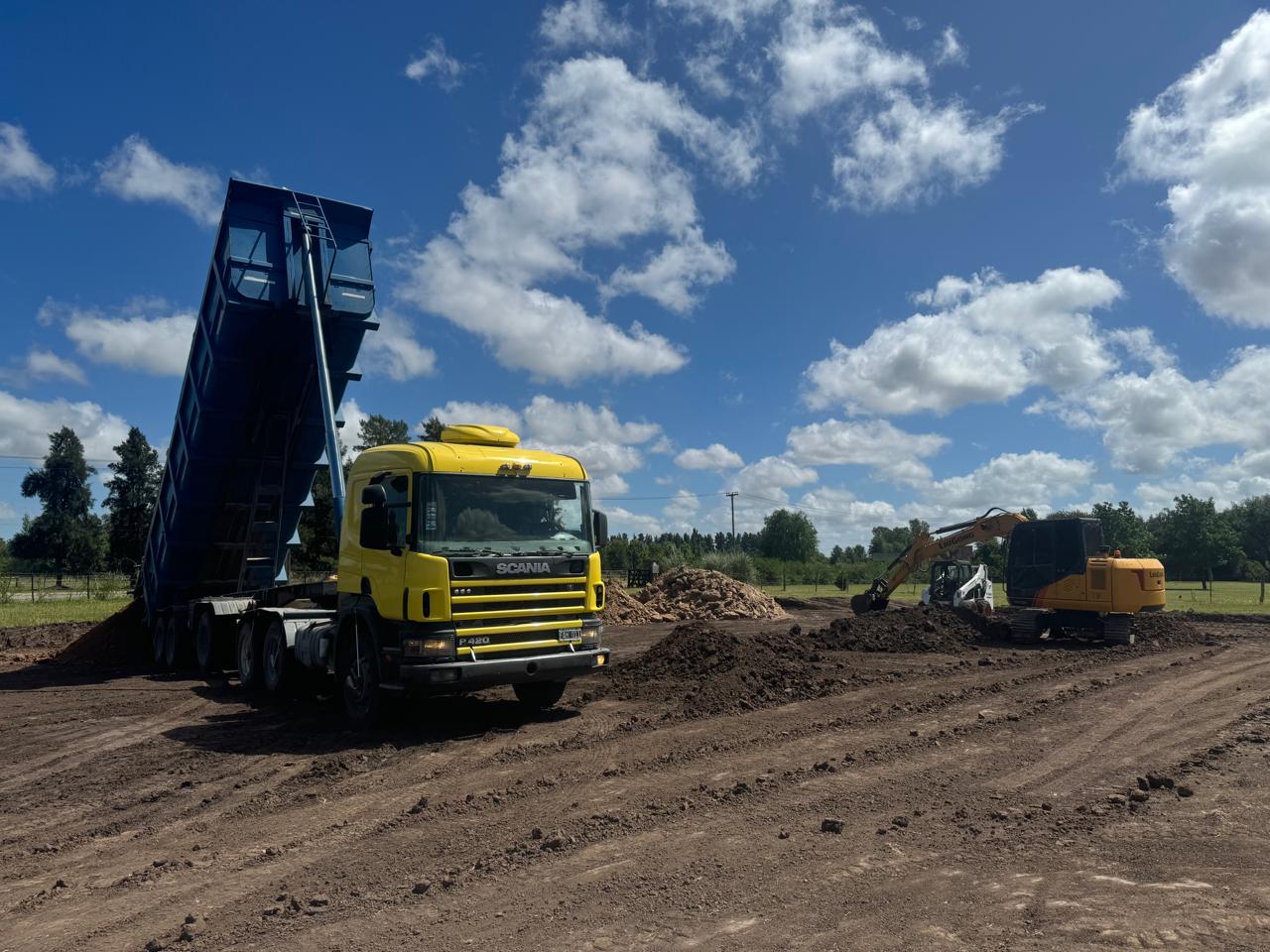 Camión volcador descargando tierra junto a una excavadora en un terreno