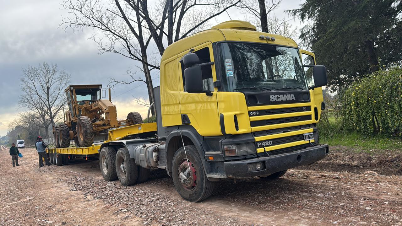 Camión Scania amarillo trasladando una motoniveladora sobre carretón